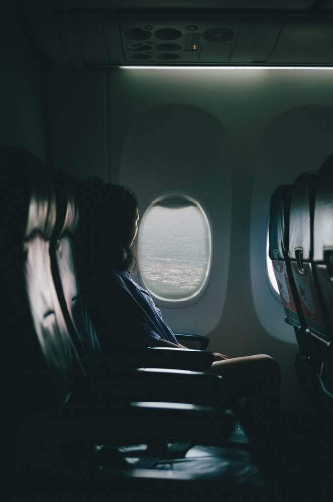 移動中の飛行機の中から窓の外を見る女性